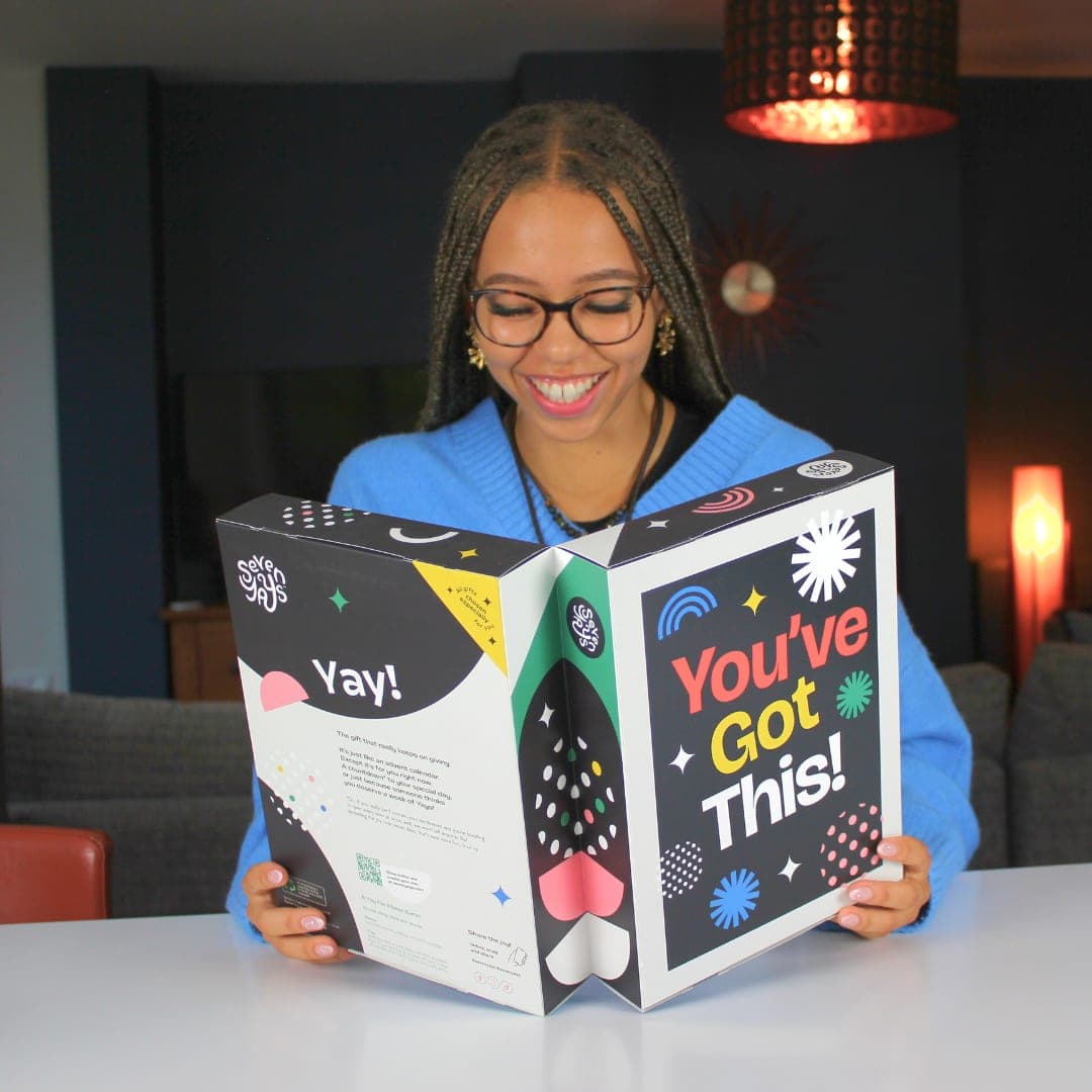 A graduate in their gown opening a Seven Yays box